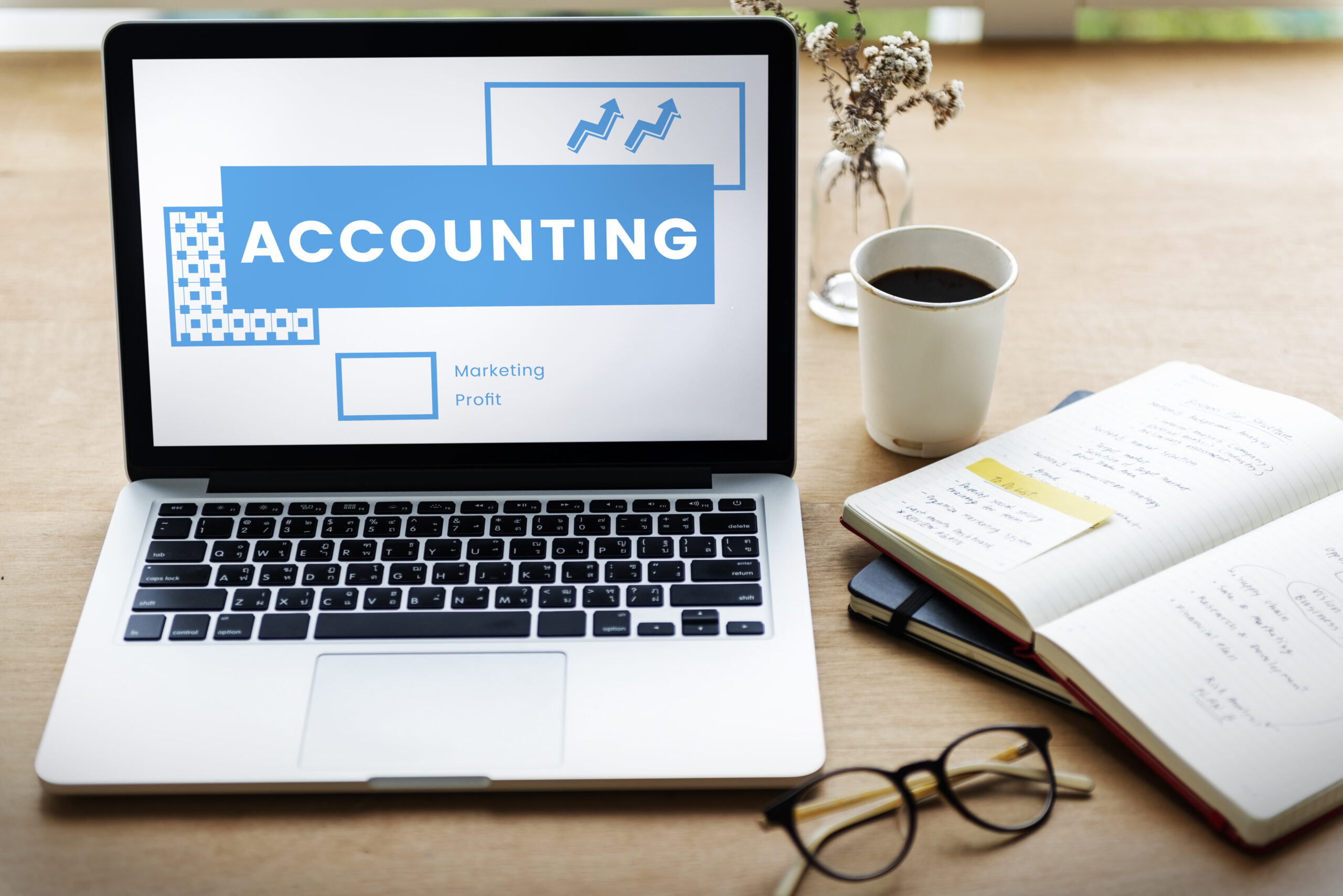 Laptop displaying the word “Accounting” on a desk with a notebook, glasses, and coffee cup, symbolizing finance and bookkeeping learning.