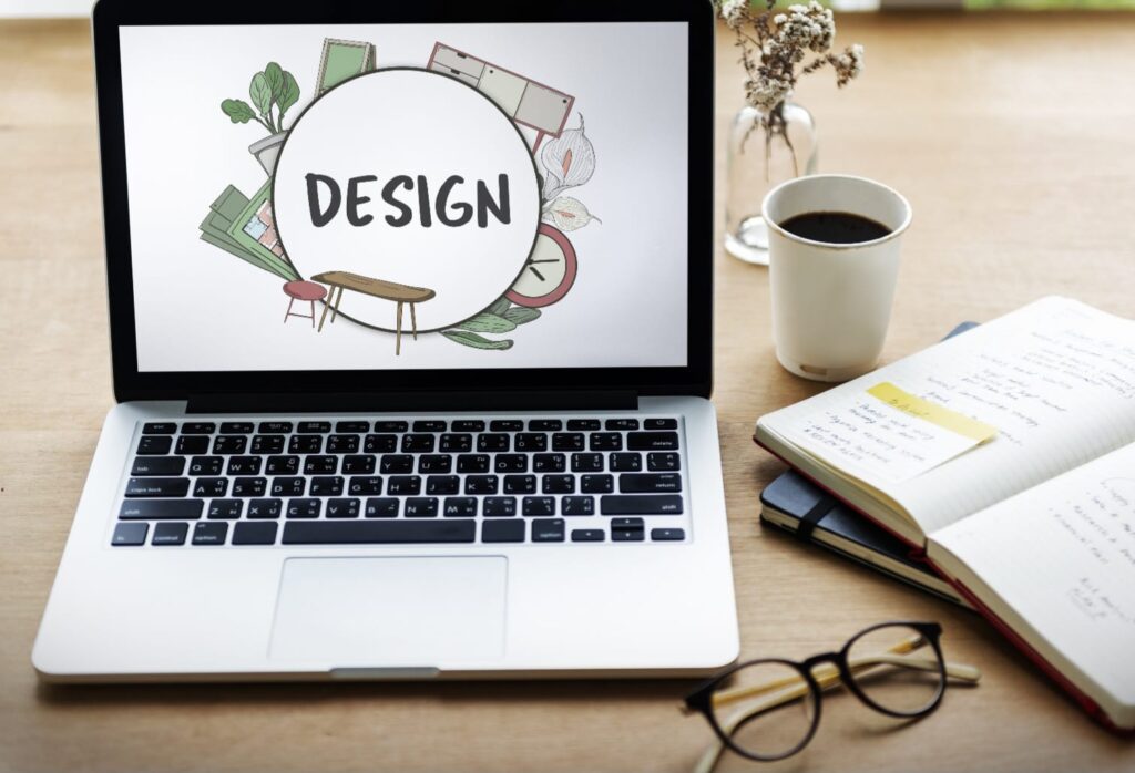 Laptop showing a design concept on screen with notebook, coffee, and glasses on a creative workspace desk.